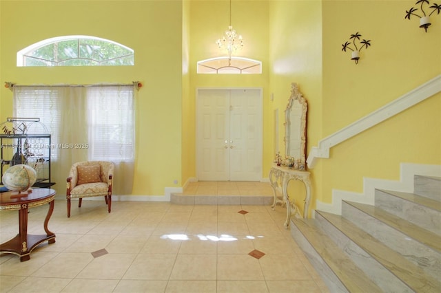 tiled entrance foyer with baseboards, stairs, a high ceiling, and a notable chandelier