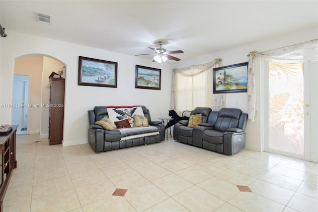 living room with arched walkways, light tile patterned floors, visible vents, and a ceiling fan