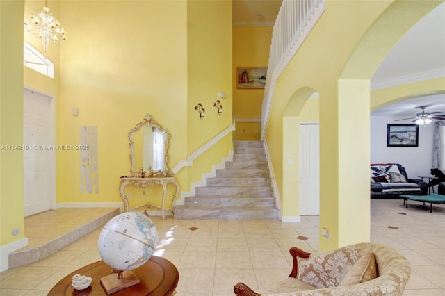 staircase featuring arched walkways, tile patterned flooring, a towering ceiling, baseboards, and crown molding