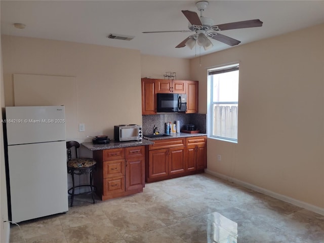 kitchen featuring backsplash, freestanding refrigerator, black microwave, brown cabinetry, and visible vents