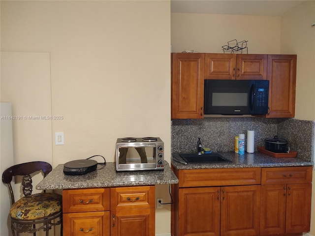 kitchen featuring black microwave, backsplash, a sink, and brown cabinetry