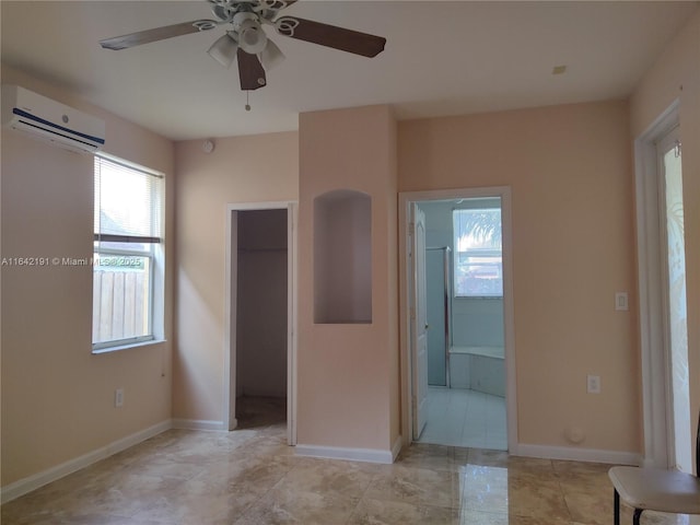 unfurnished bedroom featuring a closet, an AC wall unit, ceiling fan, ensuite bath, and baseboards