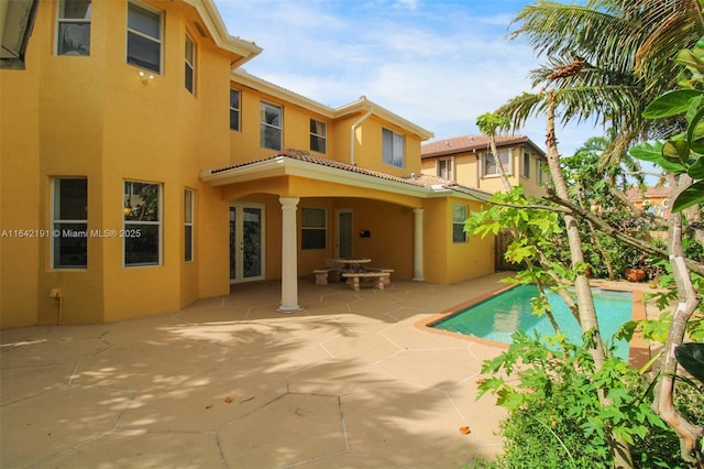 rear view of house with a tiled roof, an outdoor pool, stucco siding, and a patio
