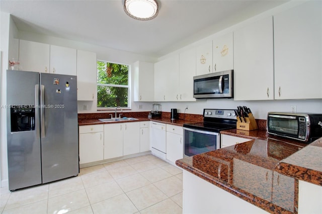 kitchen with appliances with stainless steel finishes, sink, dark stone countertops, white cabinets, and light tile patterned floors