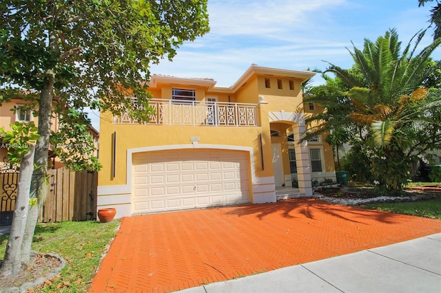 view of front of property featuring stucco siding, fence, an attached garage, a balcony, and decorative driveway