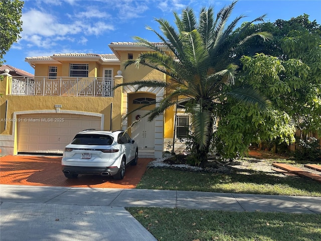 mediterranean / spanish-style home featuring a balcony, a tiled roof, an attached garage, decorative driveway, and stucco siding