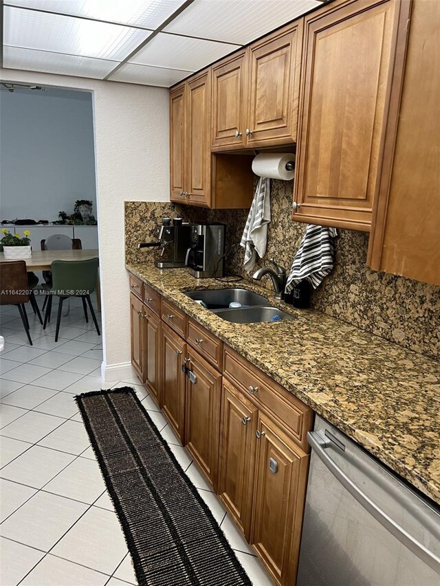 kitchen featuring dark stone countertops, light tile patterned flooring, stainless steel dishwasher, tasteful backsplash, and sink