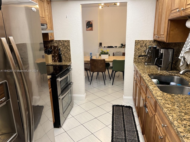 kitchen with tasteful backsplash, appliances with stainless steel finishes, light stone countertops, light tile patterned floors, and sink