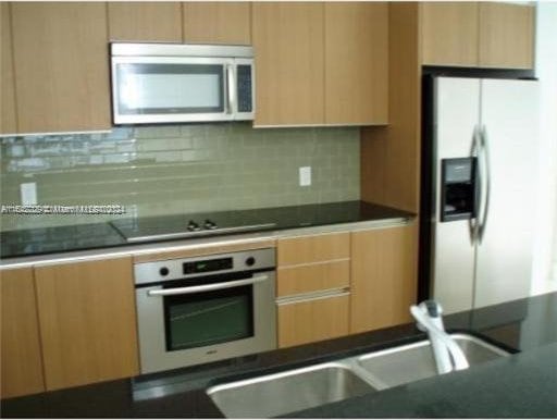 kitchen with appliances with stainless steel finishes, backsplash, and light brown cabinetry