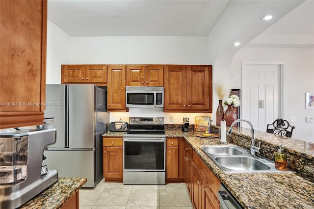 kitchen with appliances with stainless steel finishes, light tile patterned floors, sink, and dark stone countertops