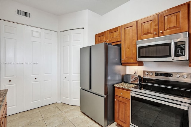 kitchen with appliances with stainless steel finishes, light tile patterned floors, and light stone countertops