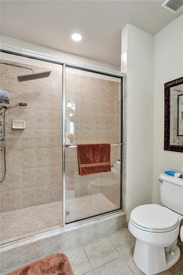 bathroom with a shower with door, toilet, and tile patterned floors