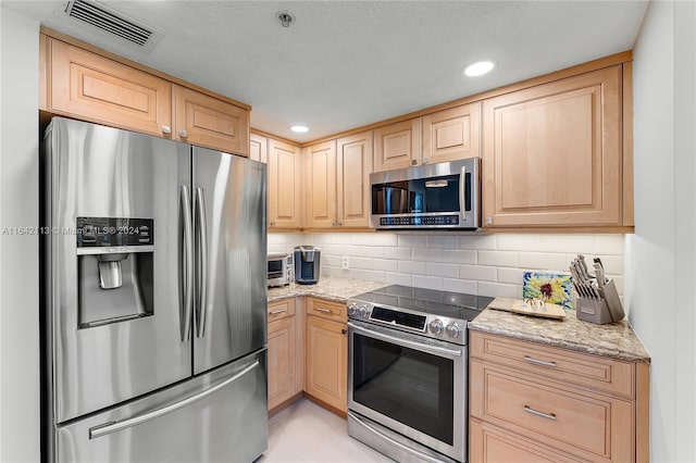 kitchen with light stone counters, stainless steel appliances, and light brown cabinetry