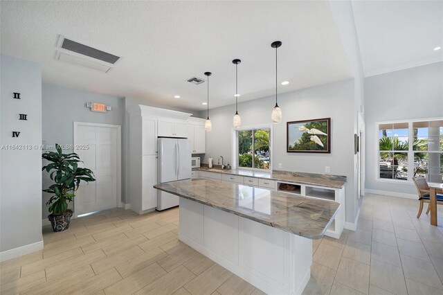 kitchen featuring white appliances, a kitchen island, white cabinetry, pendant lighting, and light stone counters