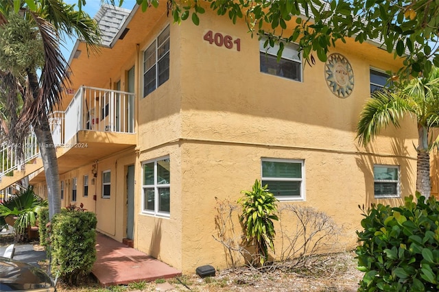 view of side of home with a balcony, roof with shingles, and stucco siding