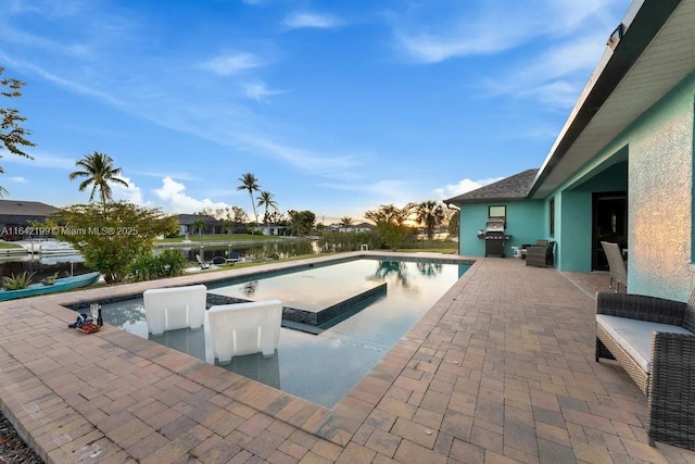 view of pool with area for grilling, a water view, and a patio