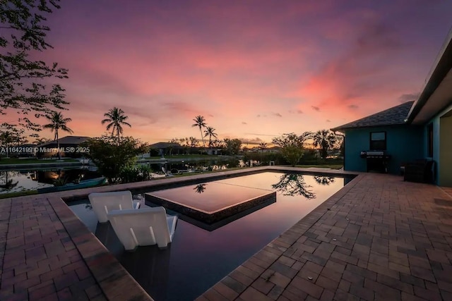 pool at dusk featuring area for grilling and a patio area