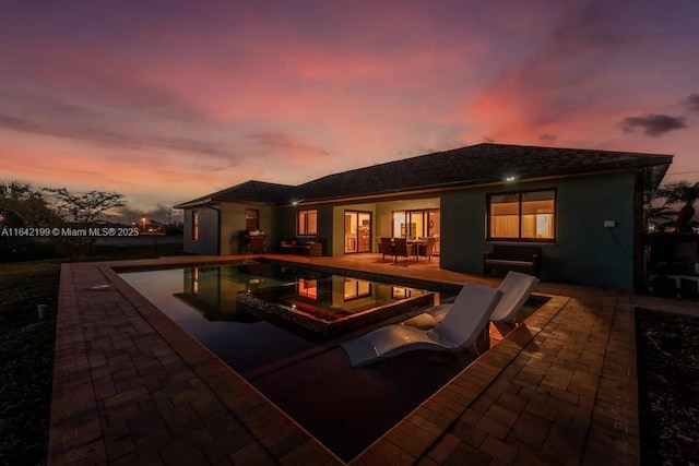 pool at dusk featuring a patio area and a jacuzzi