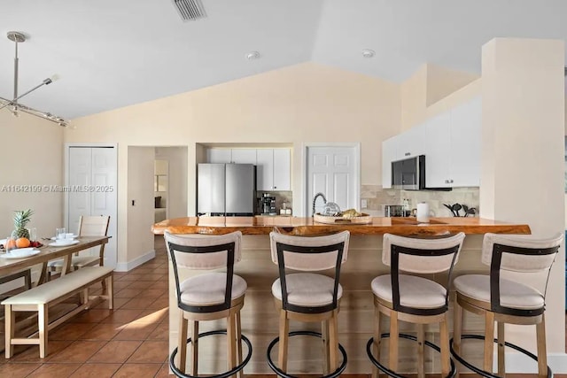 kitchen featuring kitchen peninsula, vaulted ceiling, dark tile patterned floors, tasteful backsplash, and stainless steel appliances