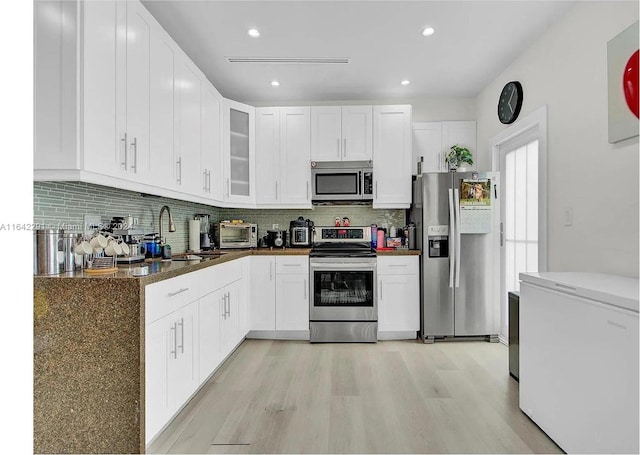 kitchen with decorative backsplash, white cabinetry, appliances with stainless steel finishes, light wood-type flooring, and sink