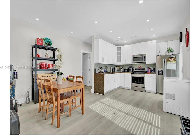 kitchen with white cabinets, light wood-type flooring, stainless steel appliances, and tasteful backsplash