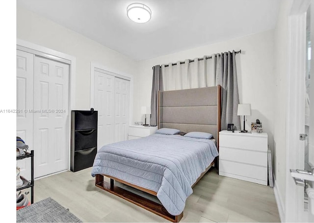 bedroom with light hardwood / wood-style flooring and multiple closets