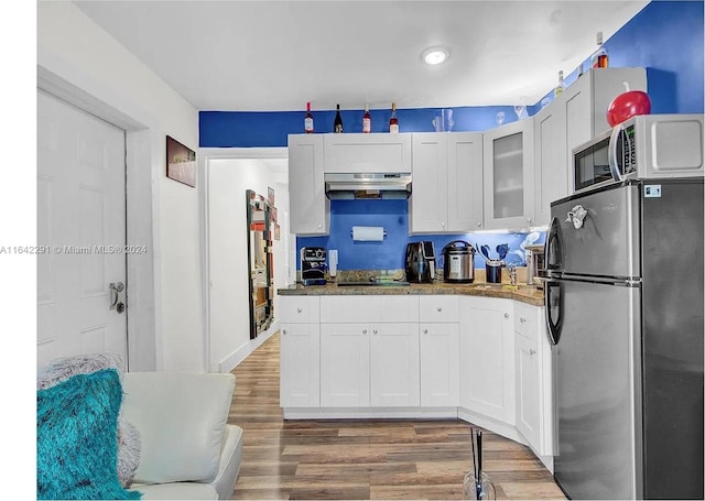 kitchen with appliances with stainless steel finishes, dark stone countertops, wood-type flooring, and white cabinets