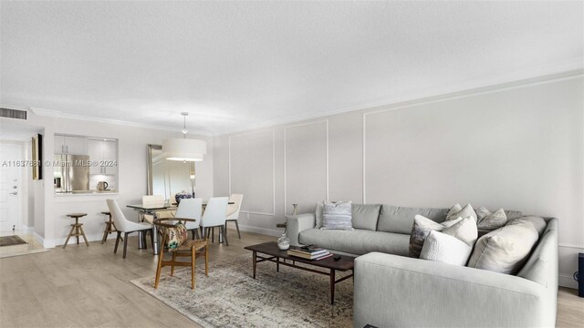 living room with a textured ceiling, crown molding, and light wood-type flooring