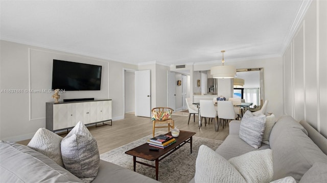 living area with light wood-type flooring, baseboards, visible vents, and ornamental molding