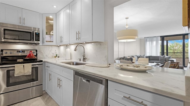 kitchen with tasteful backsplash, light stone countertops, appliances with stainless steel finishes, white cabinetry, and a sink