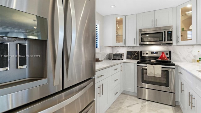 kitchen featuring marble finish floor, light stone counters, white cabinetry, stainless steel appliances, and decorative backsplash