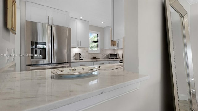 kitchen with tasteful backsplash, white cabinetry, recessed lighting, stainless steel fridge, and light stone countertops