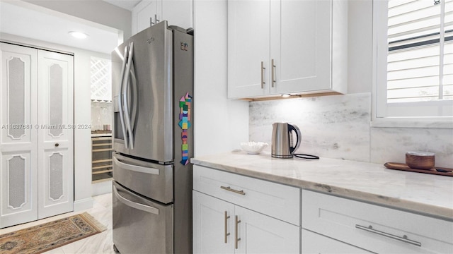 kitchen with white cabinetry, light stone counters, stainless steel refrigerator with ice dispenser, and backsplash