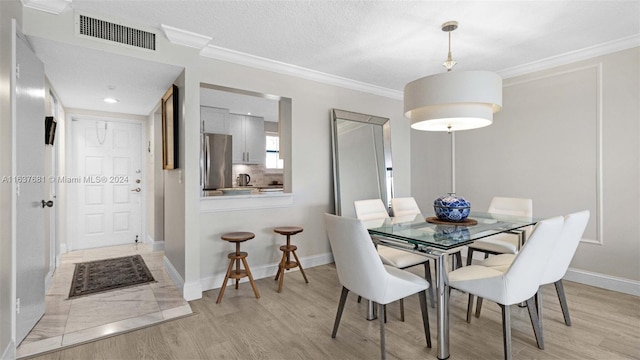 dining area featuring visible vents, light wood-style flooring, crown molding, and baseboards