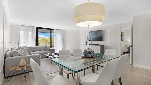 dining area featuring light wood-style flooring, baseboards, a textured ceiling, and ornamental molding