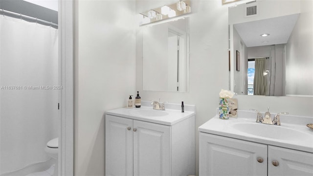 full bath with toilet, two vanities, visible vents, and a sink