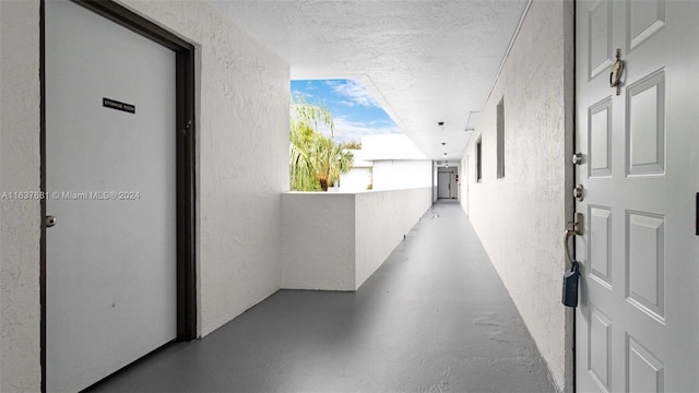 hall featuring finished concrete floors, a textured ceiling, and a textured wall