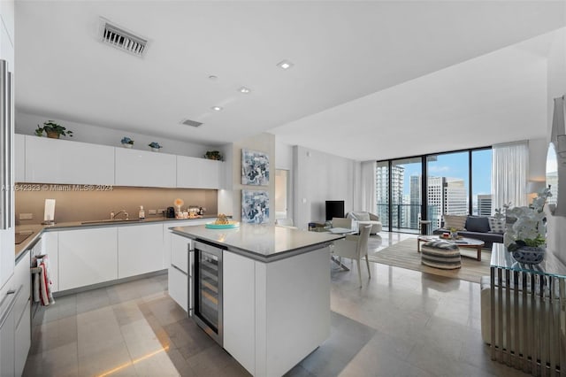 kitchen featuring a wall of windows, white cabinetry, wine cooler, a kitchen island, and sink