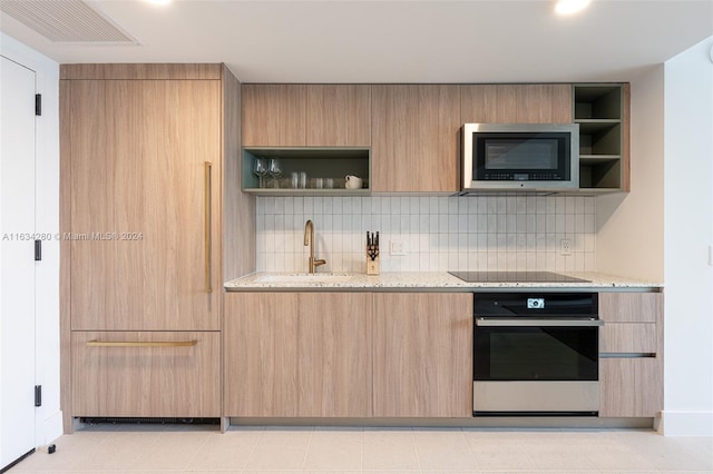 kitchen featuring backsplash, light brown cabinetry, wall oven, light stone counters, and black electric stovetop