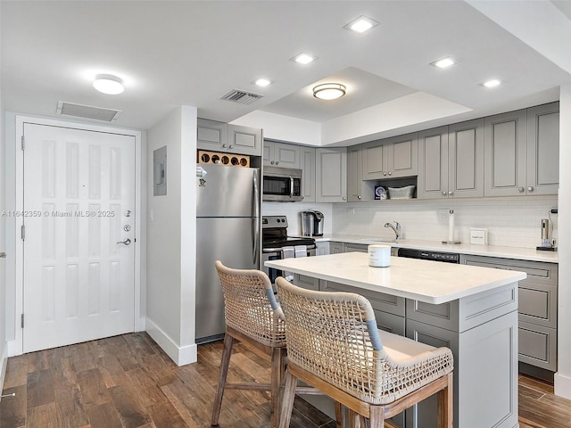 kitchen featuring gray cabinetry, sink, a center island, dark wood-type flooring, and appliances with stainless steel finishes