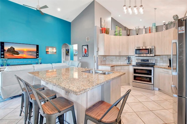 kitchen with a kitchen bar, a kitchen island with sink, high vaulted ceiling, and appliances with stainless steel finishes