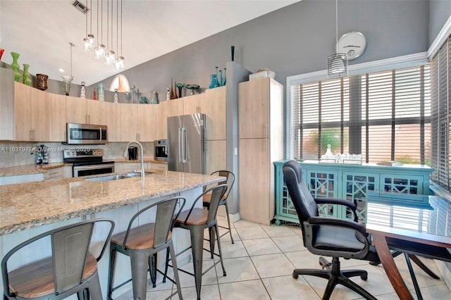 kitchen with light brown cabinets, light stone countertops, hanging light fixtures, and appliances with stainless steel finishes