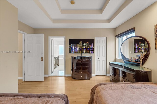 bedroom with ensuite bath, a tray ceiling, and light hardwood / wood-style floors