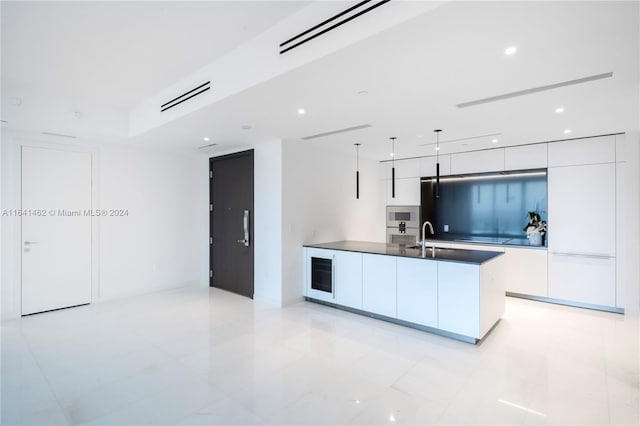 kitchen with wine cooler, white cabinets, a center island with sink, stainless steel microwave, and decorative light fixtures