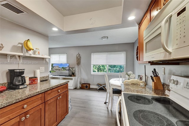 kitchen with white appliances, a tray ceiling, light hardwood / wood-style floors, and light stone countertops