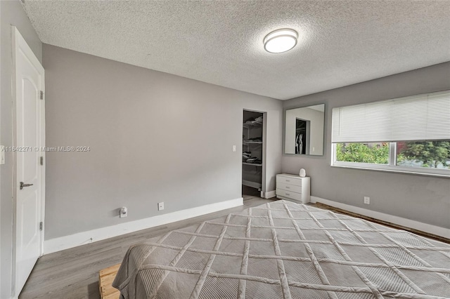 bedroom with a spacious closet, light hardwood / wood-style flooring, a textured ceiling, and a closet