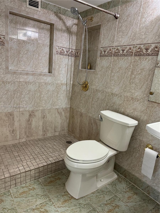 bathroom with tile walls, tiled shower, toilet, and tile patterned floors