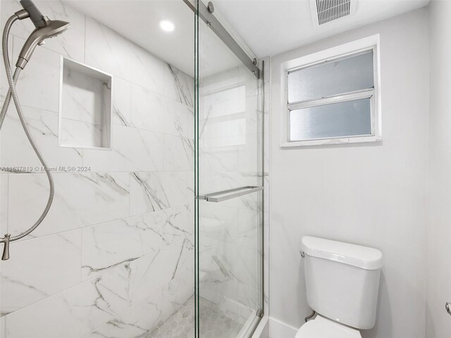 bathroom featuring a shower with door and toilet