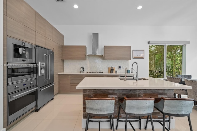 kitchen with appliances with stainless steel finishes, backsplash, wall chimney exhaust hood, sink, and light tile patterned flooring