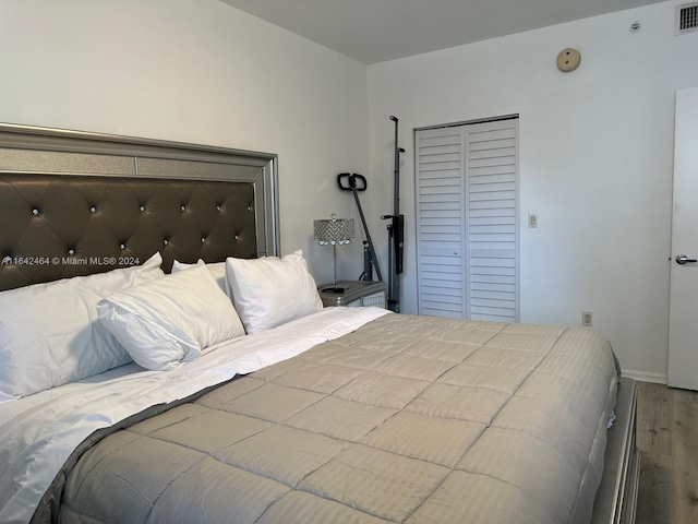 bedroom with a closet, visible vents, baseboards, and wood finished floors